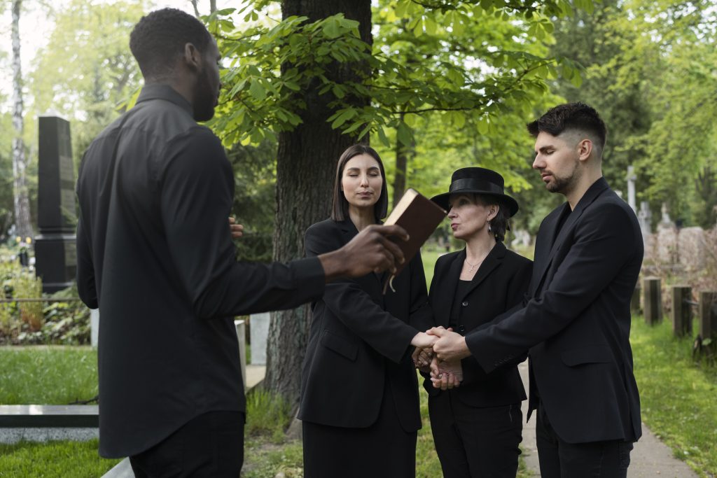 family-cemetery-holding-hands-while-priest-reads-from-bible